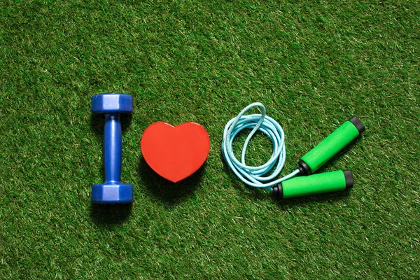 Colorful dumbbell with heart symbol and skipping rope on the grass — Stock Photo, Image