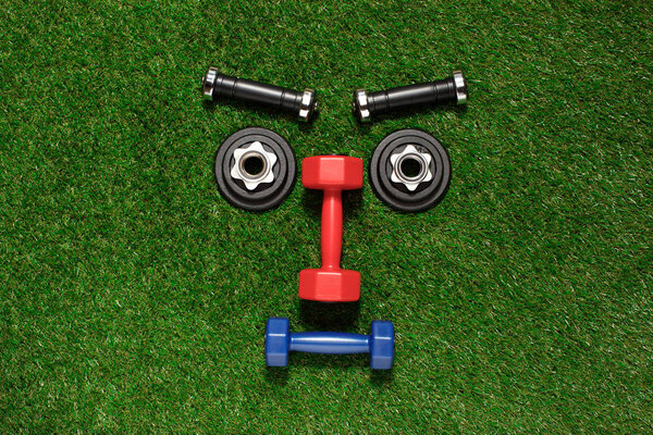 Top view of various dumbbells and weight plates in shape of serious face