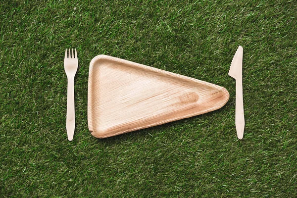 Wooden plate with fork and knife on grass — Stock Photo, Image