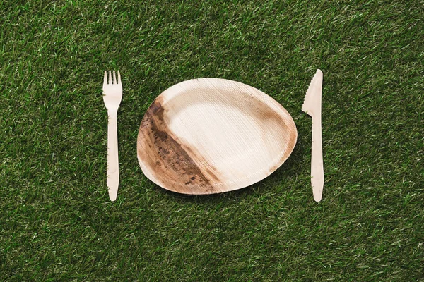 Wooden plate with fork and knife on grass — Stock Photo, Image