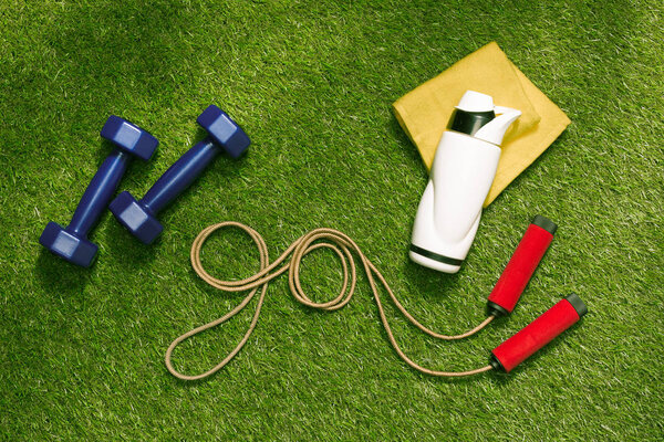 dumbbells and bottle with jump rope on grass