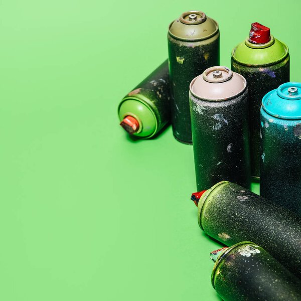 close up view of arranged cans with aerosol paint isolated on green