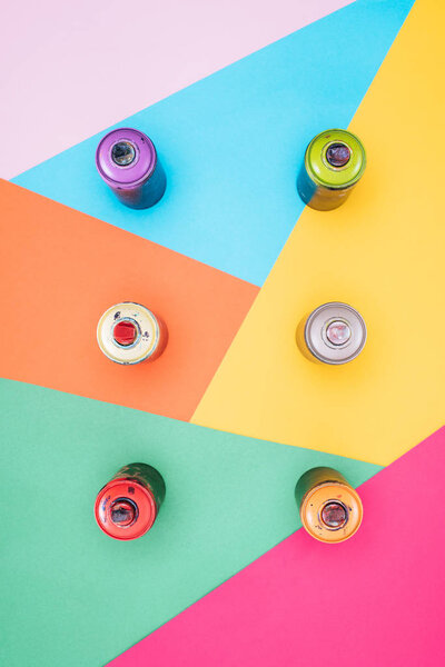 top view of arranged aerosol paint in cans on colorful background