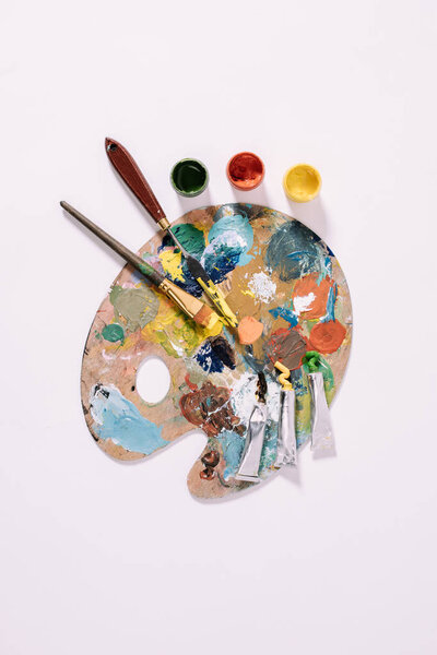 top view of palette with colorful paints and paint brushes isolated on grey 