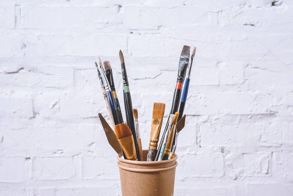 paint brushes in paper cups on white wall