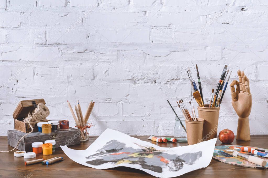 sketch and cups with brushes on wooden table in workshop