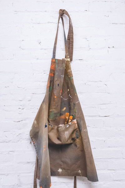 brown artist apron with paint brushes hanging on brick wall   