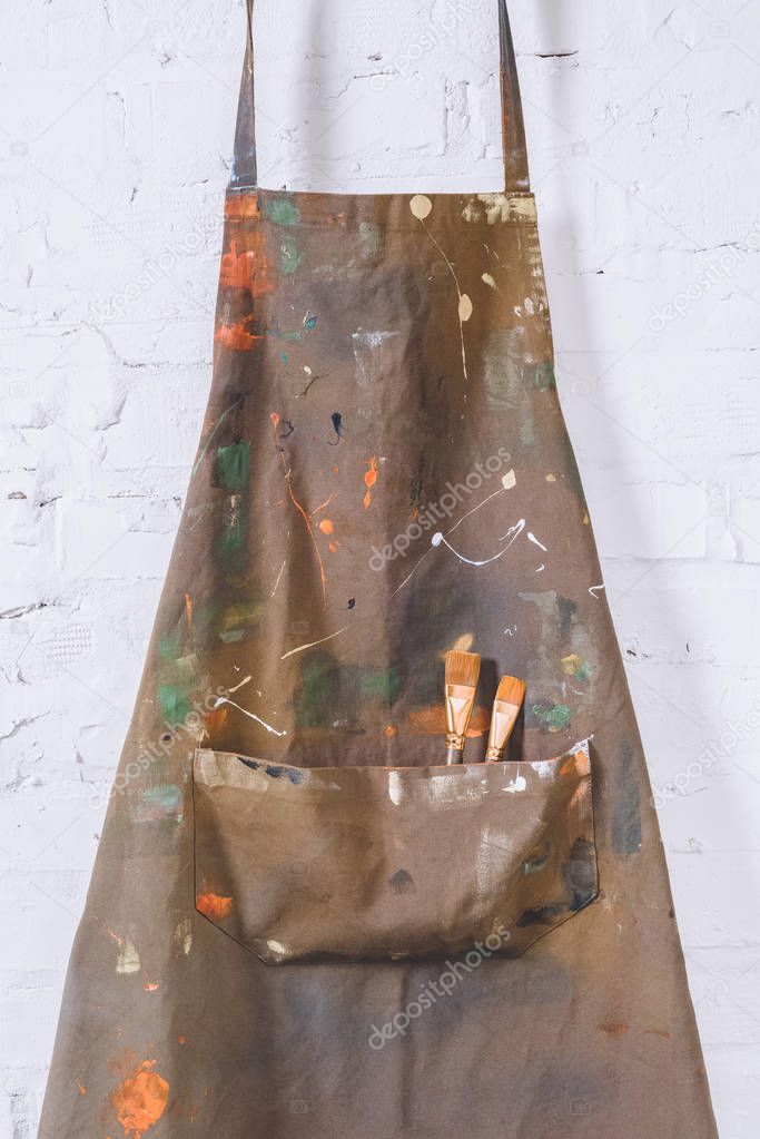 artist apron with paint brushes hanging on brick wall   
