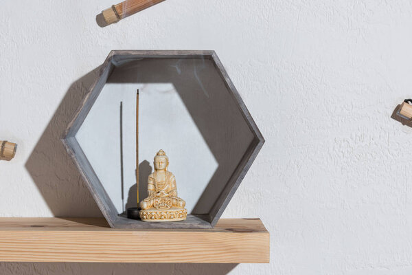 small statue of buddha in frame on wooden shelf