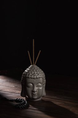 sculpture of buddha head with incense sticks on wooden table clipart