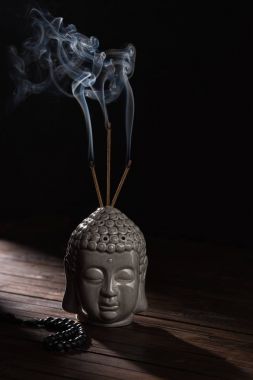 sculpture of buddha head with burning incense sticks clipart