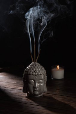 sculpture of buddha head with burning incense sticks and candle on table clipart