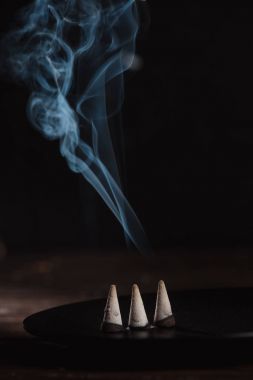 three burning incense sticks with smoke on table clipart