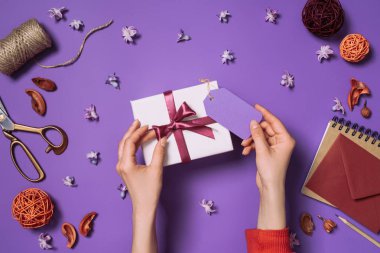 partial view of woman holding present with card isolated on purple clipart