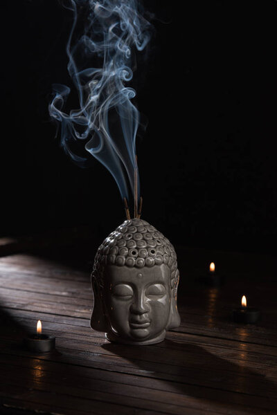 sculpture of buddha head with burning incense sticks and candles on table