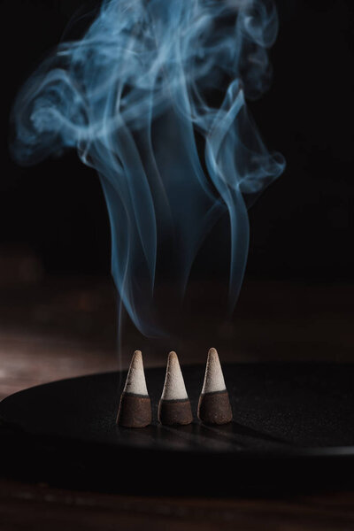 three burning incense sticks with smoke on black