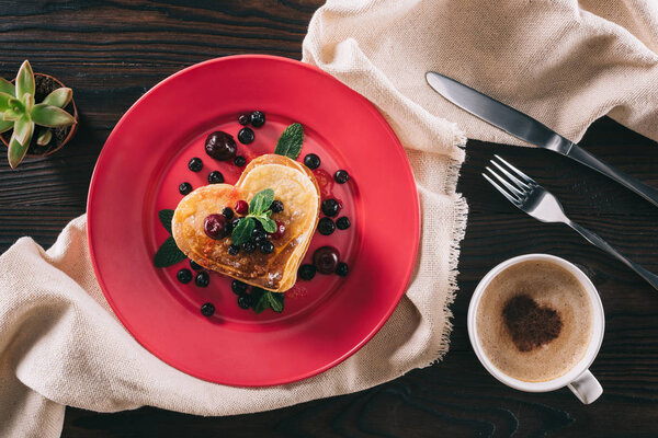 top view of heart shaped pancake with berries and mint on wooden table, valentines day concept