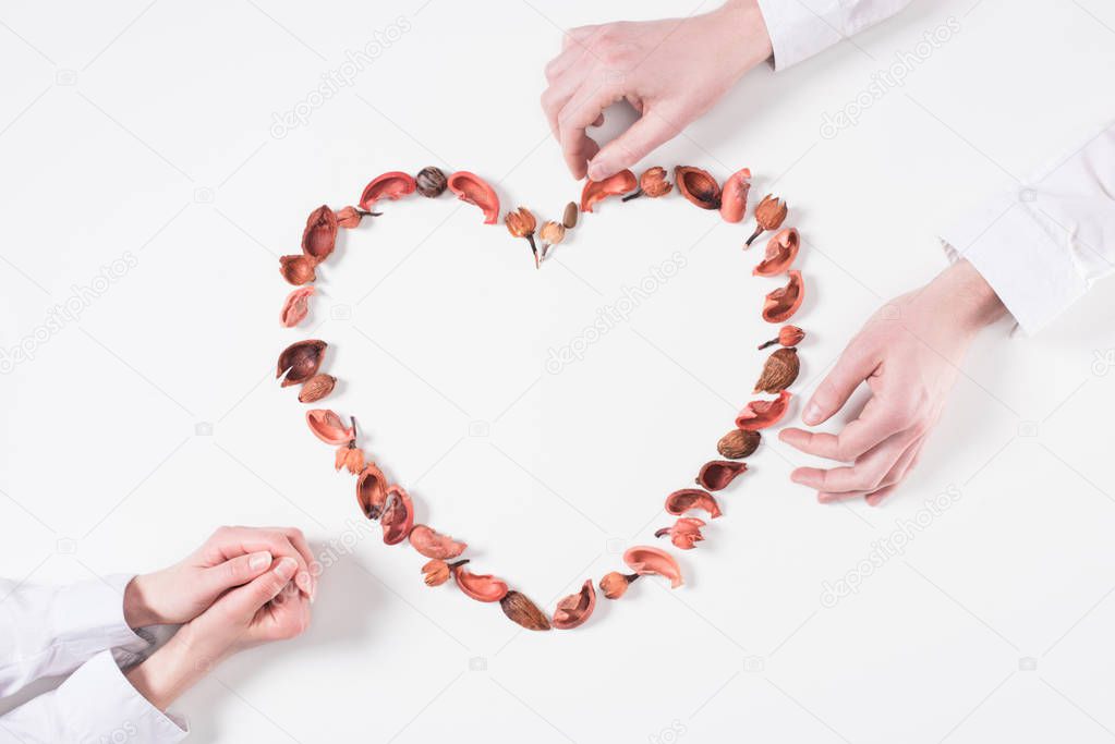 cropped image of couple making heart from dried fruits on valentines day on white