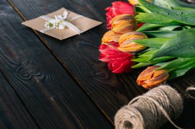 close up view of bouquet of tulips, postcard and rope on wooden tabletop clipart