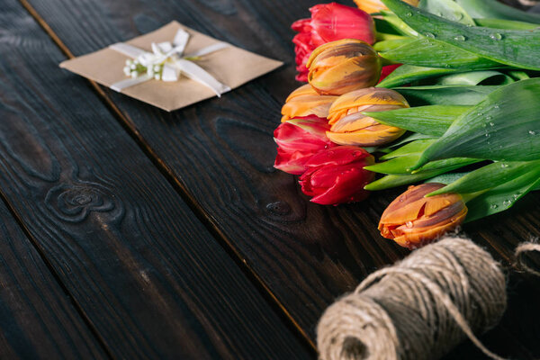 закрыть вид на букет тюльпанов, открыток и веревки на деревянном столе
