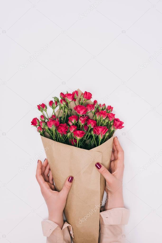 partial view of female hands and bouquet of roses in craft paper isolated on grey