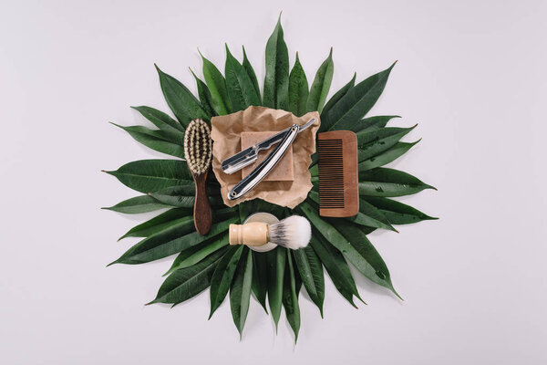 top view of arranged barber tools for shaving on green leaves isolated on grey