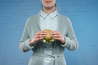 Yeşil vejetaryen burger mavi tuğla duvar önünde tutan genç kadın görüntüsünü kırpılmış