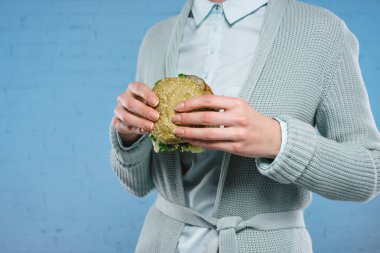 Yeşil vejetaryen burger mavi tuğla duvar önünde tutan kadın görüntüsünü kırpılmış