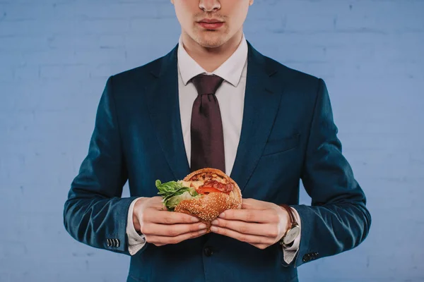 Cropped Shot Businessman Suit Holding Burger Front Blue Brick Wall — Stock Photo, Image