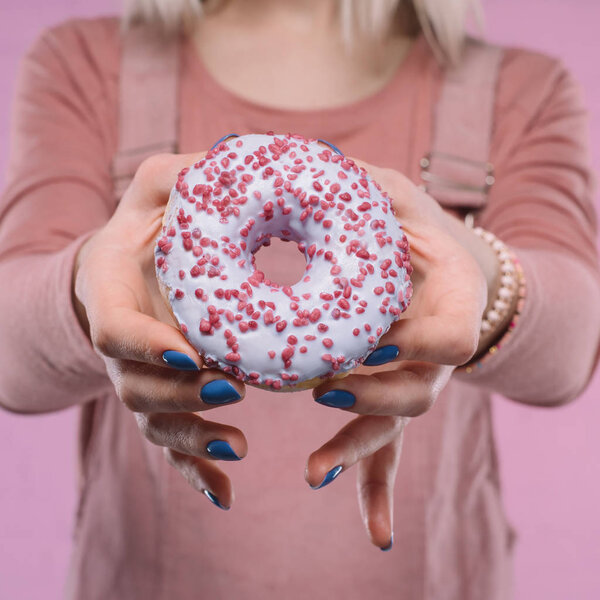 обрезанный снимок женщины, показывающей вкусный глазированный пончик на камеру
