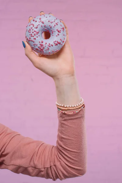 在粉红色砖墙前手持美味的琉璃甜甜圈的妇女被裁剪的镜头 — 图库照片