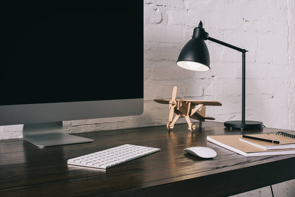 desktop computer with blank screen and wooden plane model at workplace 
