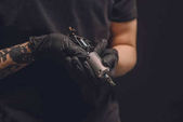 Tätowiermeister in Handschuhen hält Tinte Maschine isoliert auf schwarz