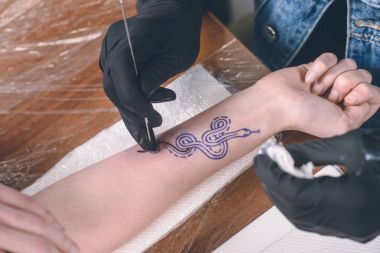 Cropped view of tattooing process on arm piece clipart