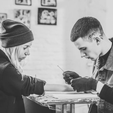 Black and white photo of tattoo artist in gloves working on female arm piece in studio clipart