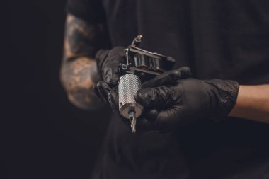 Male hands in gloves holding tattoo machine isolated on black clipart