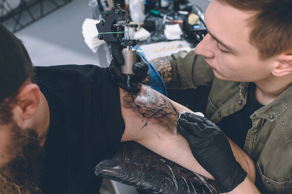 Бородатый мужчина и мастер татуировки во время процесса татуировки в студии
