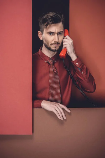 Pria Bijaksana Memegang Headset Telepon Oleh Dinding Kertas Merah Terisolasi — Foto Stok Gratis