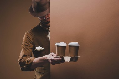 Stylish man in casual clothes holding coffee in paper cups isolated on brown