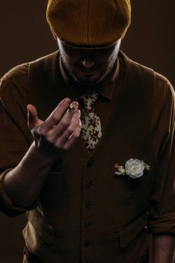 Young man in vintage styled clothes holding cigarette isolated on brown clipart