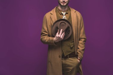 Stylish man wearing coat and holding hat isolated on purple clipart