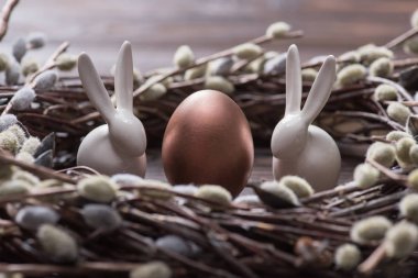 bronze easter egg and rabbits in catkins nest on table clipart
