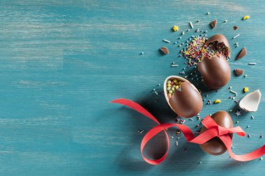 top view of broken chocolate easter eggs on turquoise surface clipart