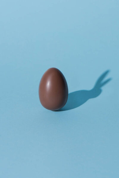 one chocolate easter egg with bunny shadow on blue surface