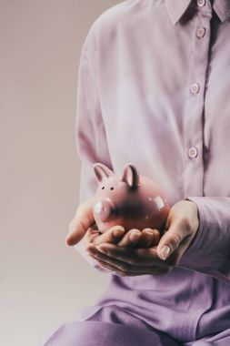 partial view of woman holding pink piggy bank in hands isolated on lilac clipart