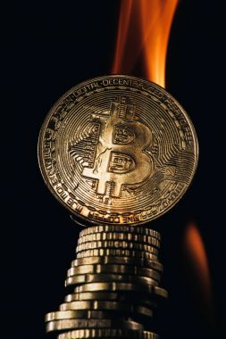 Close up view of golden bitcoins and fire isolated on black clipart