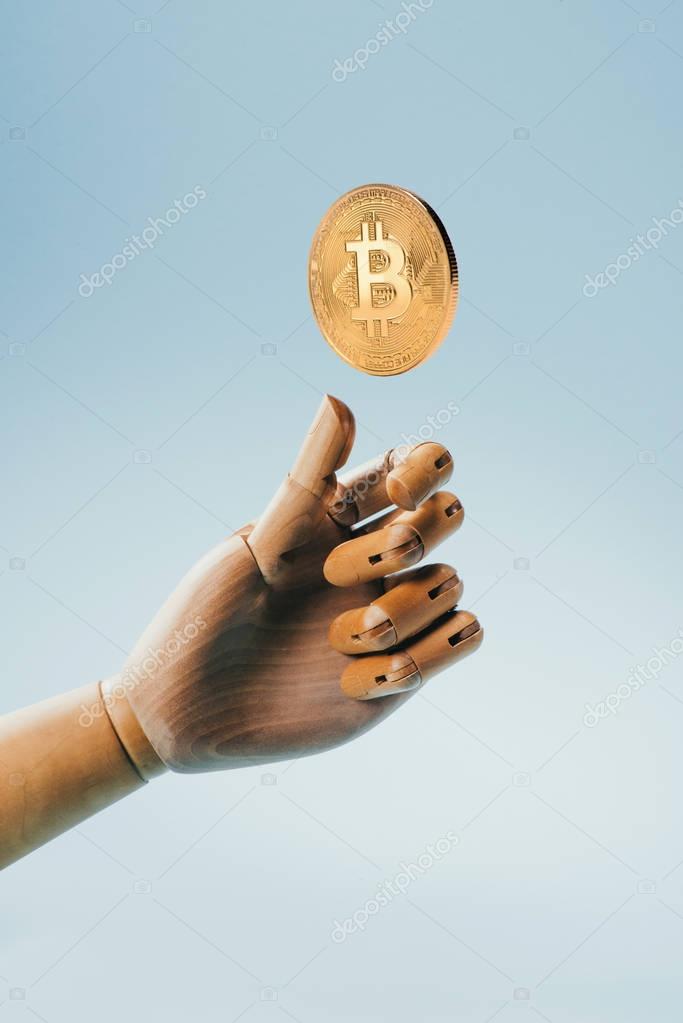 Close up view of wooden puppet hand and golden bitcoin isolated on blue