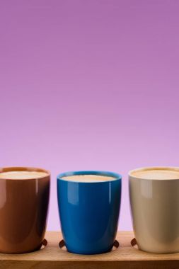 close up view of colorful cups of coffee isolated on purple clipart