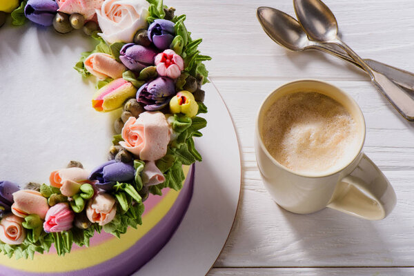 Закрыть вид на чашку кофе и цветочный украшенный торт на белой деревянной поверхности
