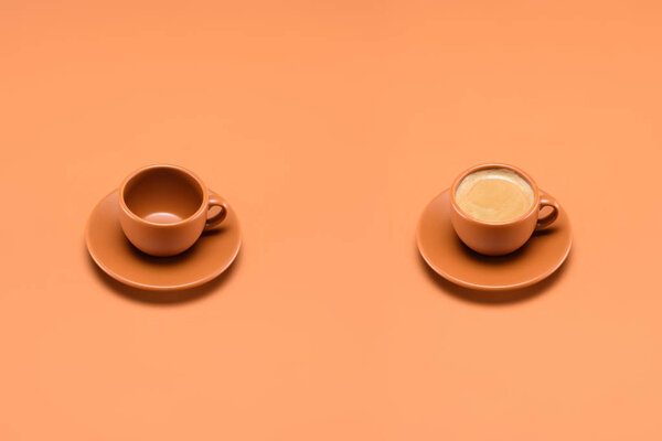 close up view of empty cup and cup of coffee isolated on peach
